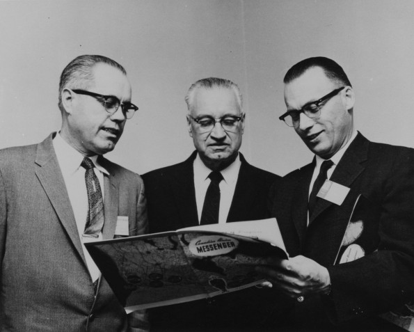 R. C. Spanger, W. B. Ochs, and J. W. Bothe looking at an issue of the Canadian Union Messenger, 1960s