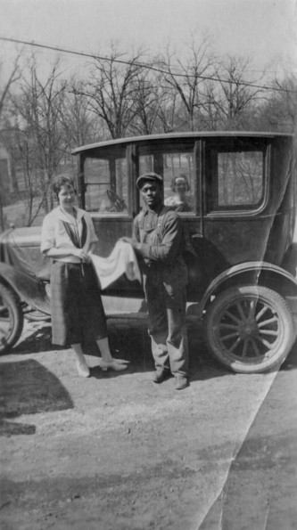Woman and a mechanic pose in front of a 1920's era automobile