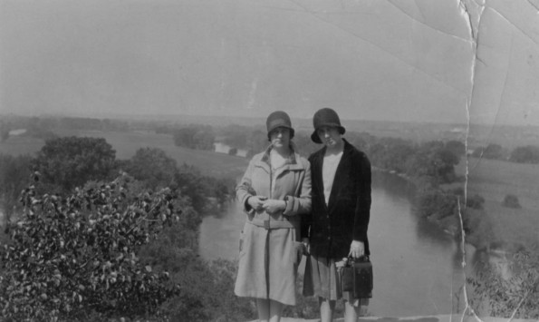 Two unknown women pose on a bluff overlooking a river or small lake