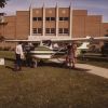 Four people observing a plane in front of the Johnson Gymnasium Andrews University