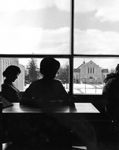 Andrews University students studying at the James White Library with Pioneer Memorial Church visible out of the window behind them