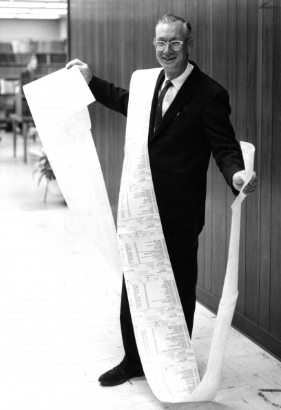 [Leonard Hill standing with the 22-foot length invoice for the 1,194 magazines and periodicals to which the James White Library subscribes]