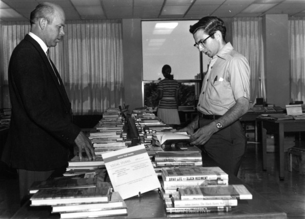 [Richard Powell assisting someone at the book exhibit in the James White Library]