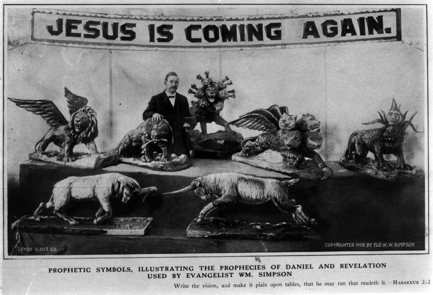 Man in suit standing with papier-mâché beasts under a banner that reads "Jesus is Coming Again."